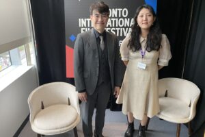 Ryoo Seung-wan stands beside Grace Han in front of a poster for Toronto International FIlm Festival.