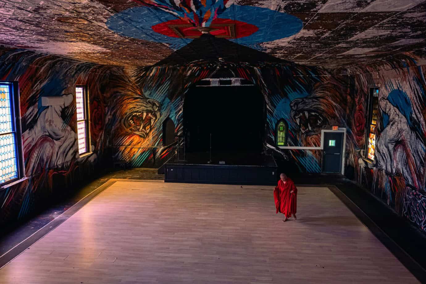 Movie still for Abiding Nowhere, a robed monk in a room with floor to ceiling murals