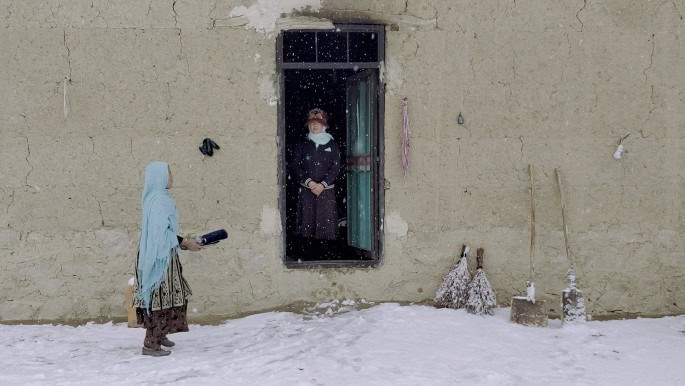 Still for Kamay of a woman walking past another standing in doorway, with snow on the ground