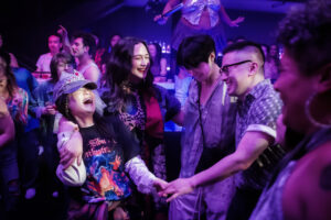 Kelly Marie Tran, Lily Gladstone, Han Gi-chan, and Bowen Yang dance together in a circle in a nightclub.