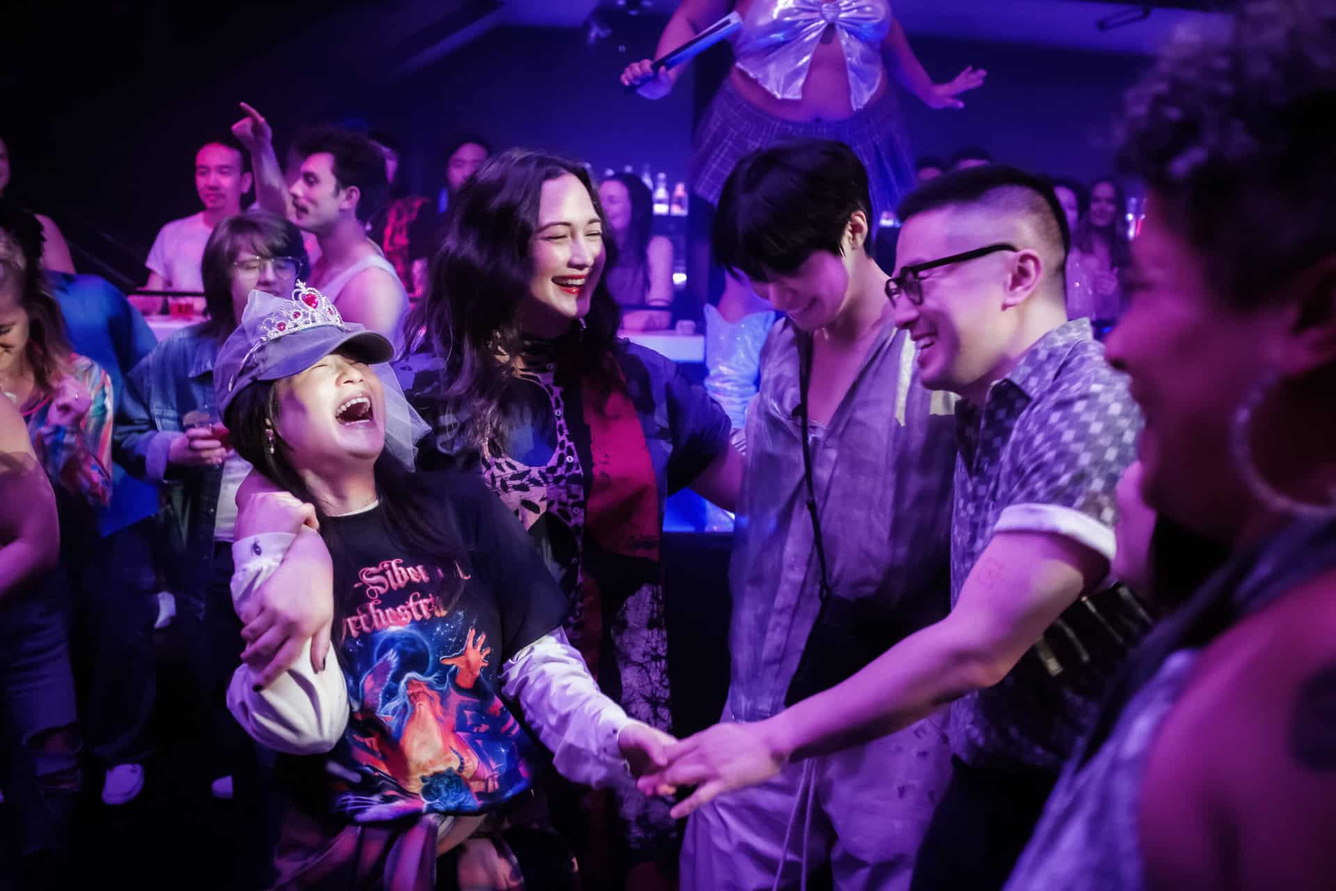 Kelly Marie Tran, Lily Gladstone, Han Gi-chan, and Bowen Yang dance together in a circle in a nightclub.
