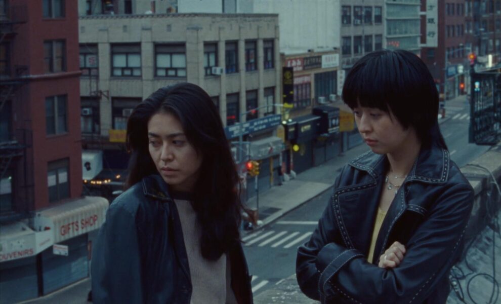 Mei and her friend look off-screen on a balcony/fire escape in New York.