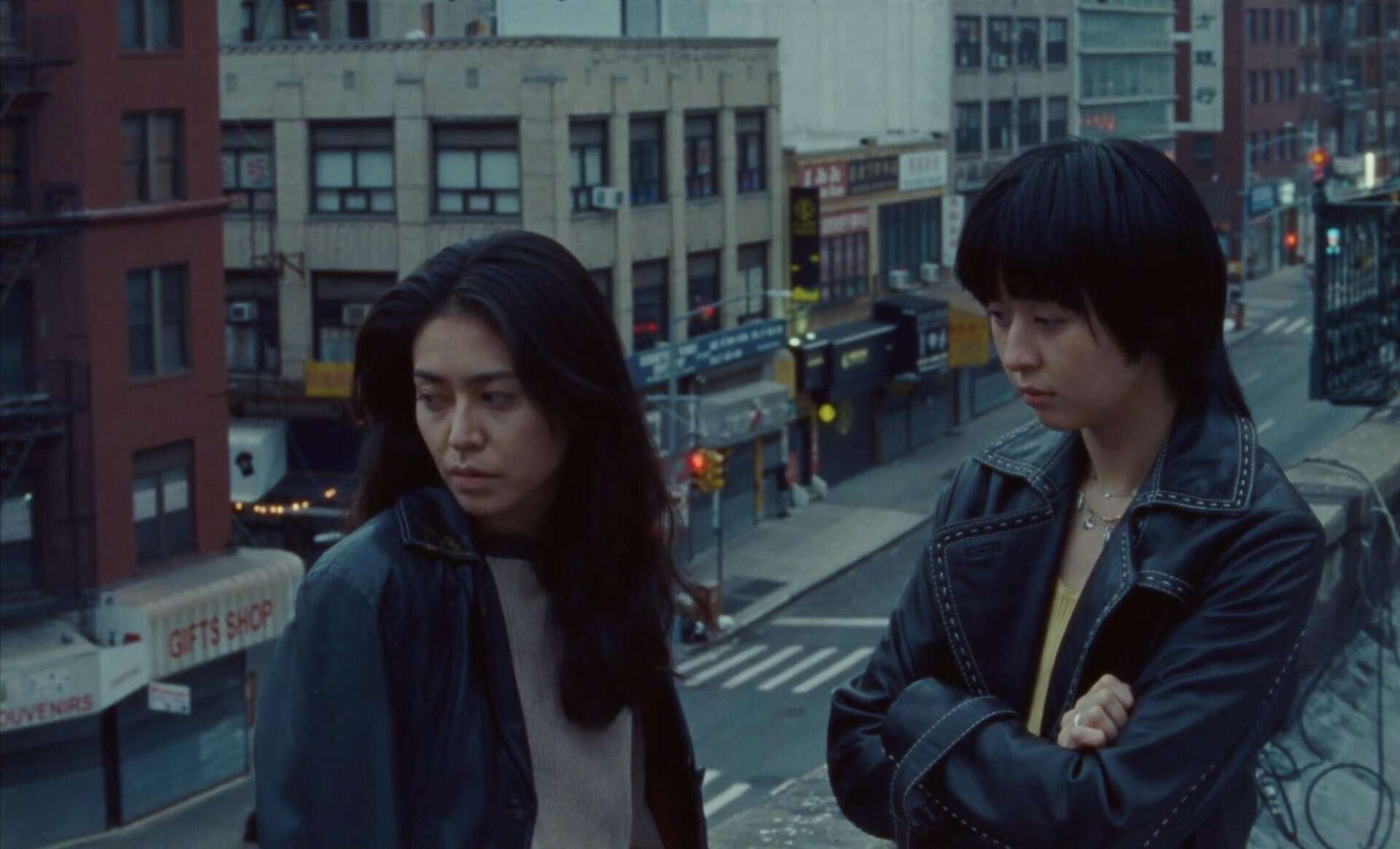 Mei and her friend look off-screen on a balcony/fire escape in New York.